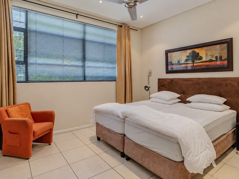 A well-maintained bedroom featuring tiled flooring, a ceiling fan, and a built-in desk, complemented by large windows with venetian blinds.