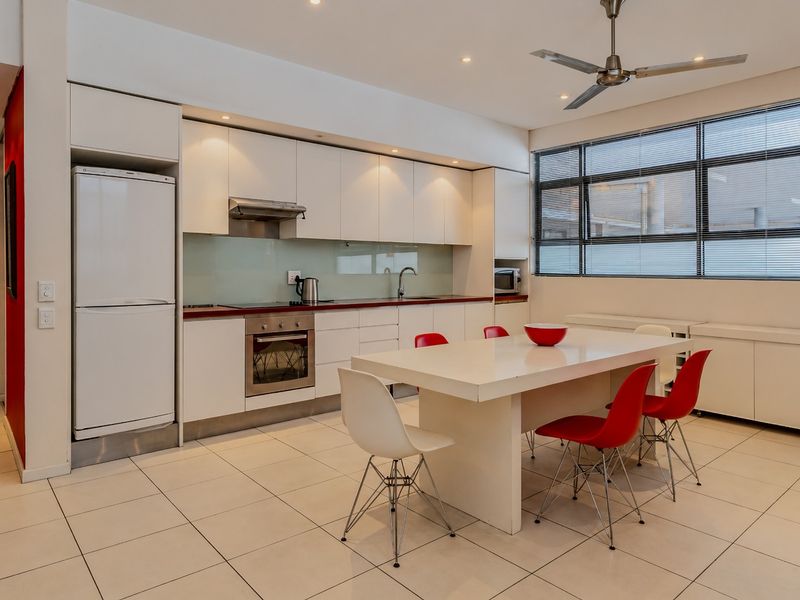 Modern open-plan kitchen and dining area featuring sleek white cabinetry, integrated appliances, tiled flooring, and large windows providing ample natural light.
