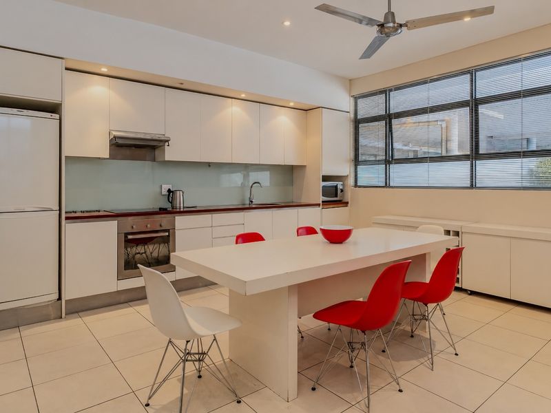 Modern open-plan kitchen and dining area featuring sleek white cabinetry, integrated appliances, tiled flooring, and a large window providing ample natural light.