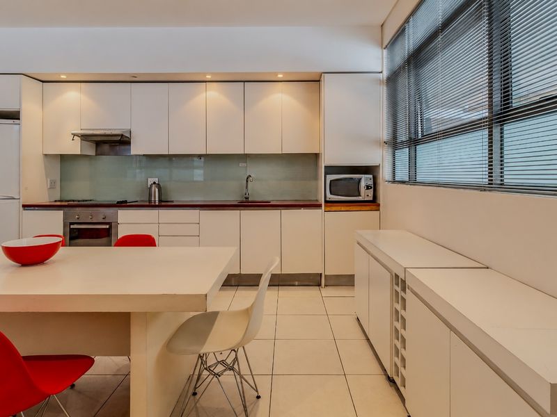 Modern kitchen featuring white cabinetry, integrated appliances, tiled flooring, and large windows with venetian blinds, offering a clean and functional culinary space.