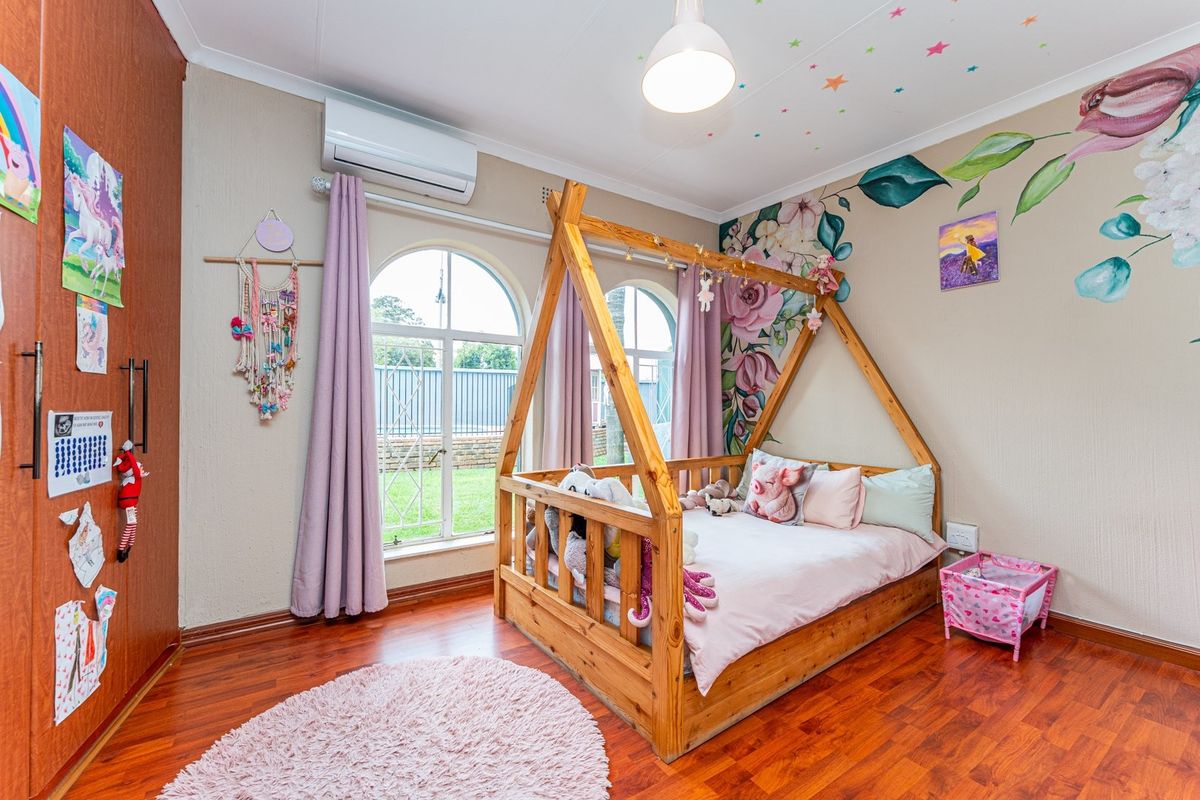 A well-maintained bedroom featuring laminate flooring, arched windows, a built-in wardrobe, and a split-system air conditioner for climate control.