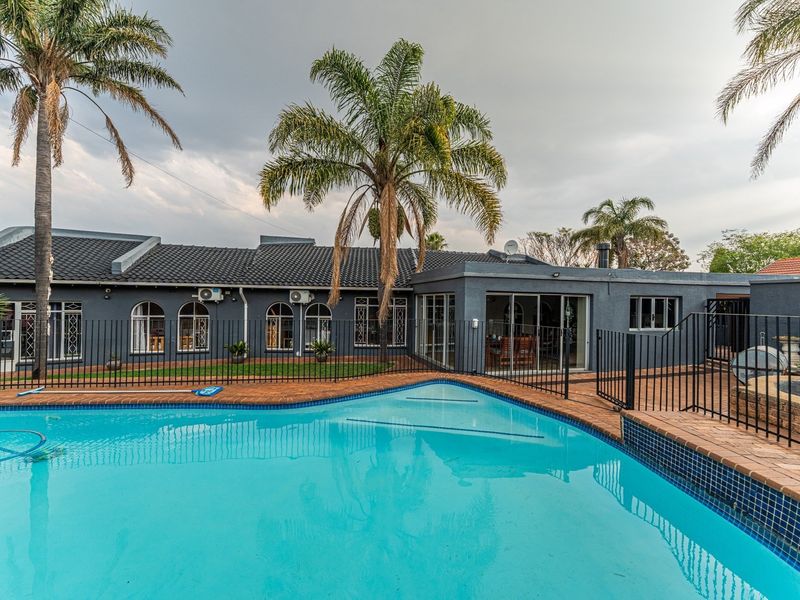 A well-maintained outdoor pool area featuring a swimming pool with brick paving, metal safety fencing, and views of the rear house elevation.