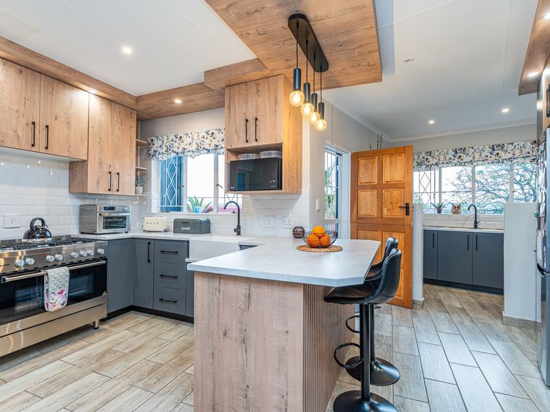 Modern kitchen featuring wood-tone and grey cabinetry, a central island with breakfast bar, gas stove, and high-quality finishes throughout.