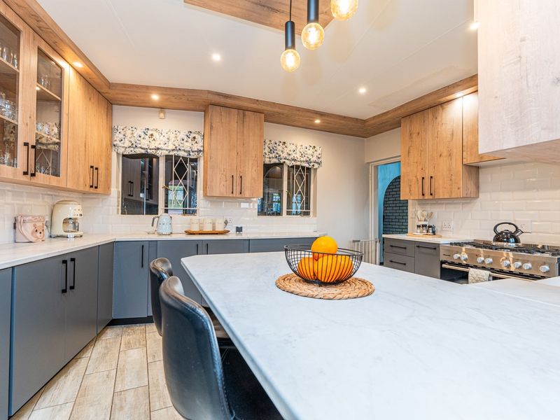 Modern kitchen featuring wood-tone and grey cabinetry, stone countertops, subway tile backsplash, and a central island with integrated gas stove and stylish pendant lighting.