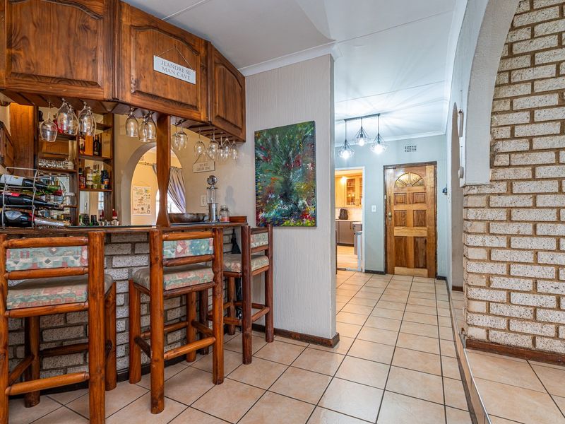 A dedicated home bar area featuring a built-in wooden counter, overhead glass storage, and a rustic brick feature wall, leading to the main entrance.