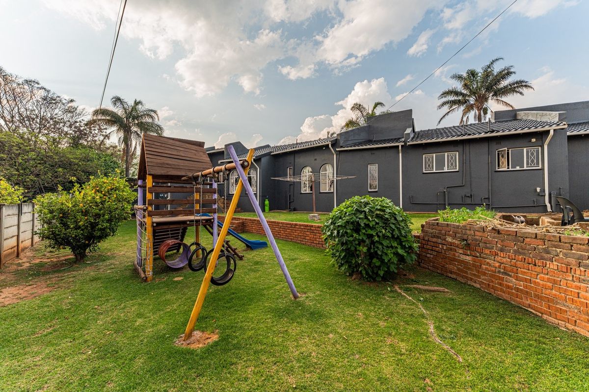 Rear garden view featuring a lawn, brick retaining wall, and the rear elevation of the house with security-fitted windows.