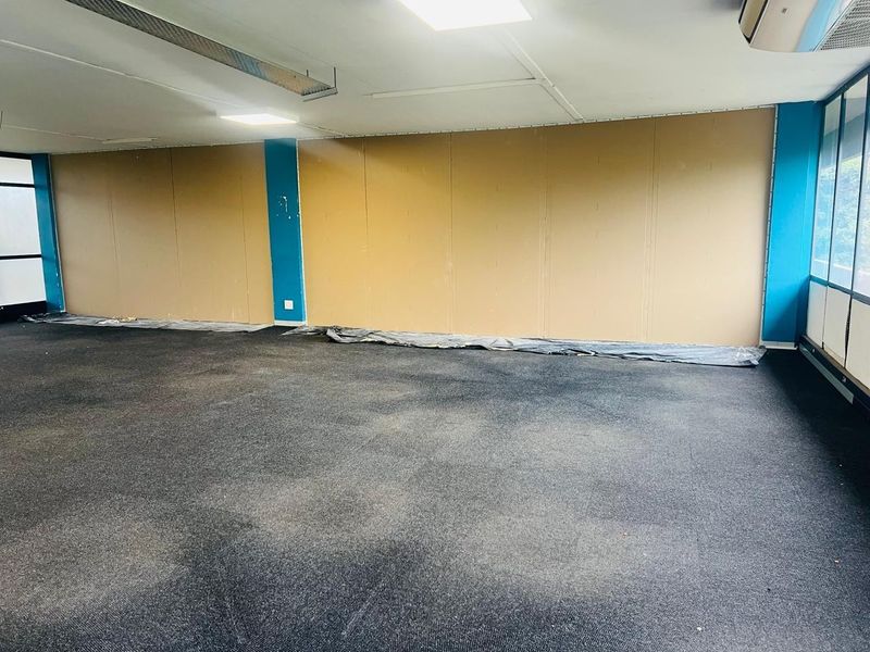 An empty office space featuring recessed ceiling lights, wall-mounted air conditioning, and carpeted flooring, currently in need of cosmetic refurbishment.