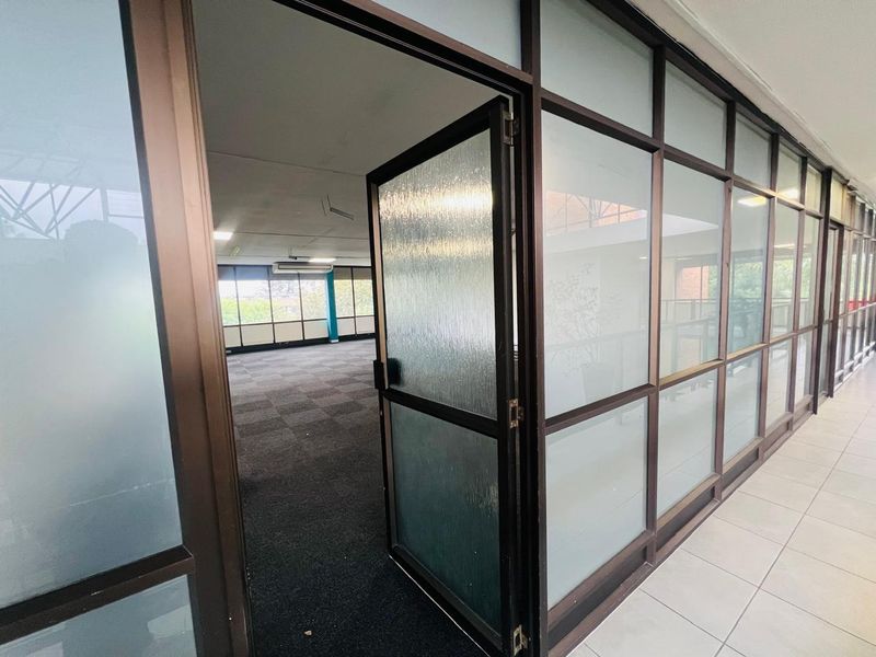 An open-plan office space featuring aluminium-framed glass partitioning, carpeted flooring, and a suspended ceiling with integrated air conditioning.