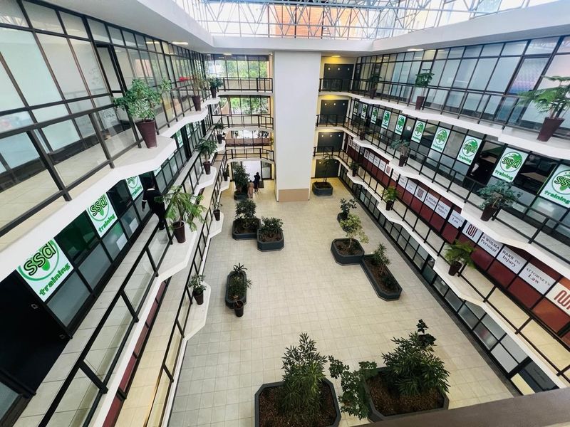 A bright, multi-level office atrium featuring a large skylight, tiled flooring, and glass-walled office suites arranged around a central open space.