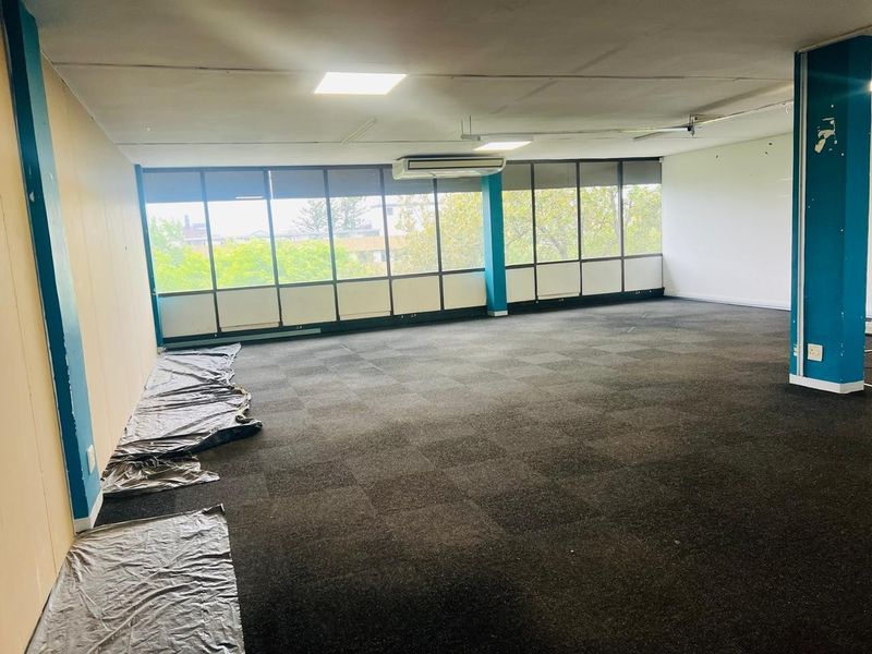 An empty, open-plan office space featuring large windows, carpeted flooring, and ceiling-mounted air conditioning, offering a blank canvas for professional workspace customization.