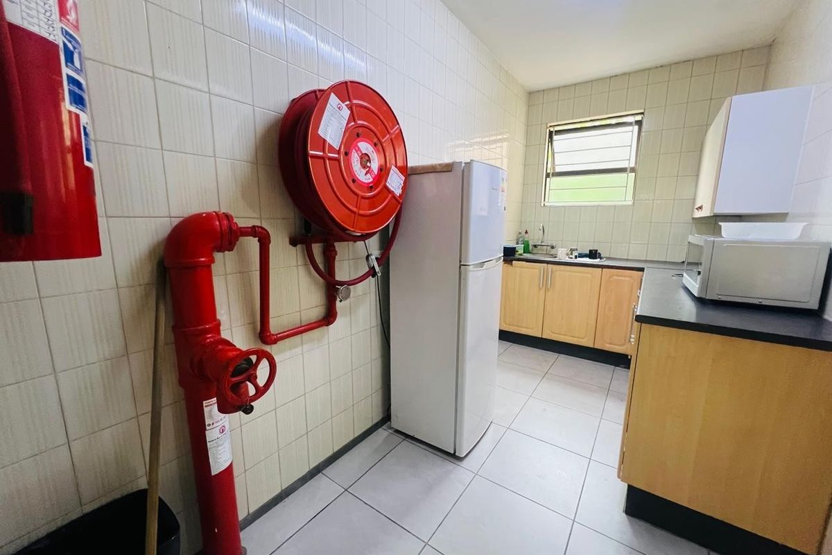 Functional office kitchen area featuring tiled walls, laminate cabinetry, stainless steel sink, and integrated fire safety equipment including a hose reel and hydrant.