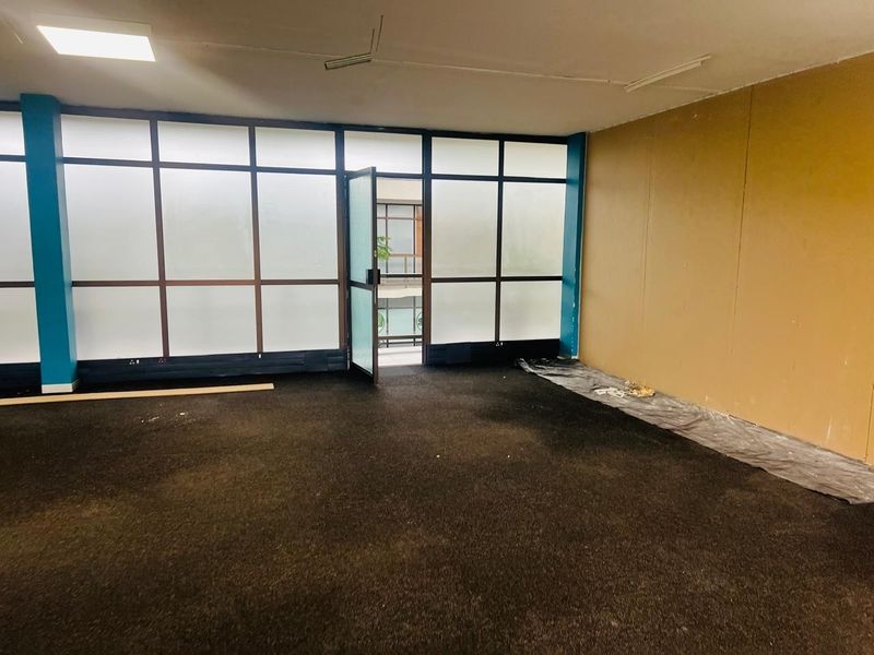 An empty office space featuring dark carpeting, a frosted glass partition wall, and neutral-toned walls, suitable for a professional workspace renovation.