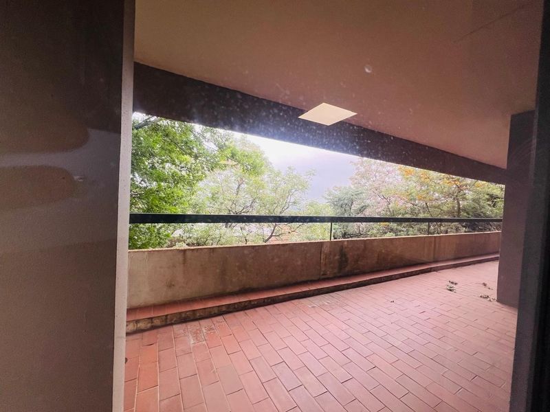 A covered balcony featuring tiled flooring, a metal safety railing, and a view of surrounding trees.