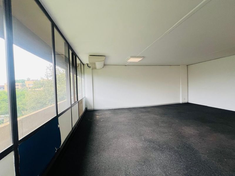 An empty office space featuring large windows, carpet flooring, and a wall-mounted air conditioning unit.