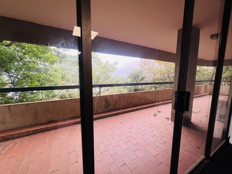 A spacious covered balcony featuring terracotta tiled flooring, a metal balustrade, and a concrete parapet wall, offering an elevated outdoor area.
