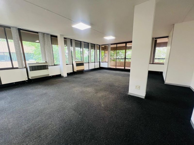 Spacious, empty office suite featuring large windows, carpeted flooring, built-in air conditioning units, and access to a private balcony.