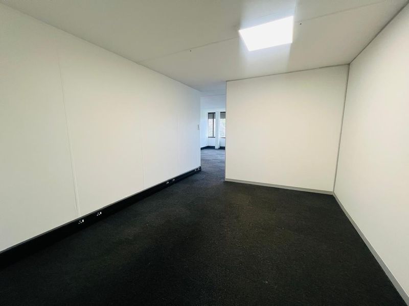 A clean, empty office space featuring dark carpet flooring, white walls, and integrated skirting board trunking for electrical connectivity.