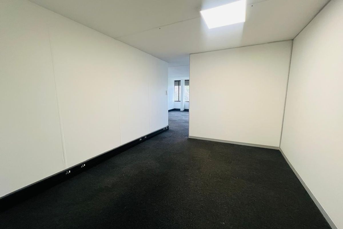 A clean, empty office space featuring dark carpet flooring, white walls, and integrated skirting board trunking for electrical connectivity.