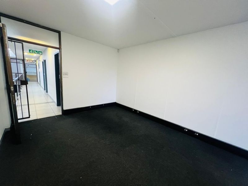 An empty office space featuring a skylight, black carpeting, and a security gate entrance, suitable for a professional workspace.