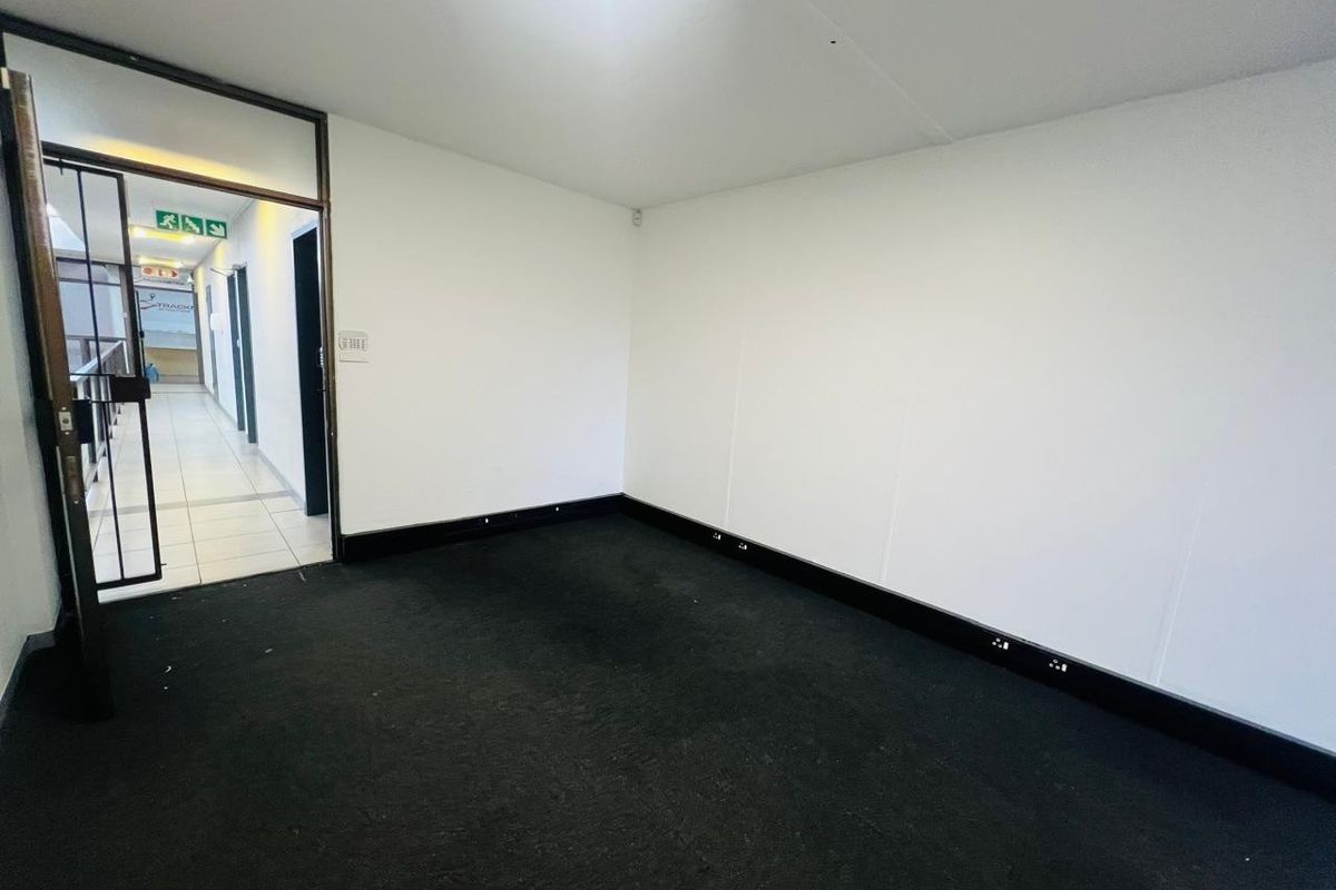 An empty office space featuring a skylight, black carpeting, and a security gate entrance, suitable for a professional workspace.