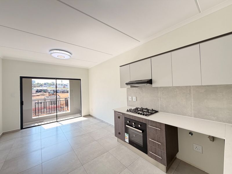 Modern open-plan kitchen and living area featuring sleek cabinetry, built-in gas hob, oven, and direct access to a private balcony.
