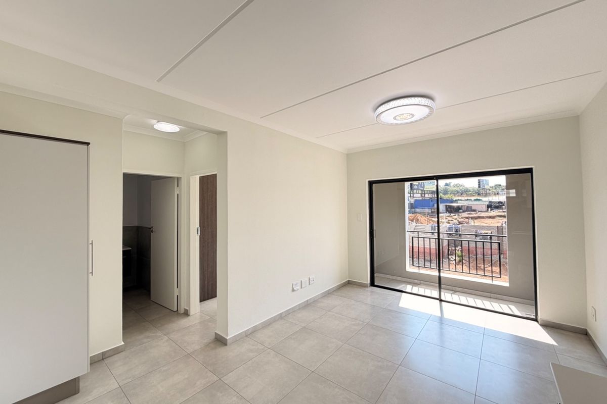A bright, empty living area featuring neutral tiled flooring, a built-in cupboard, and a sliding glass door leading to a balcony.
