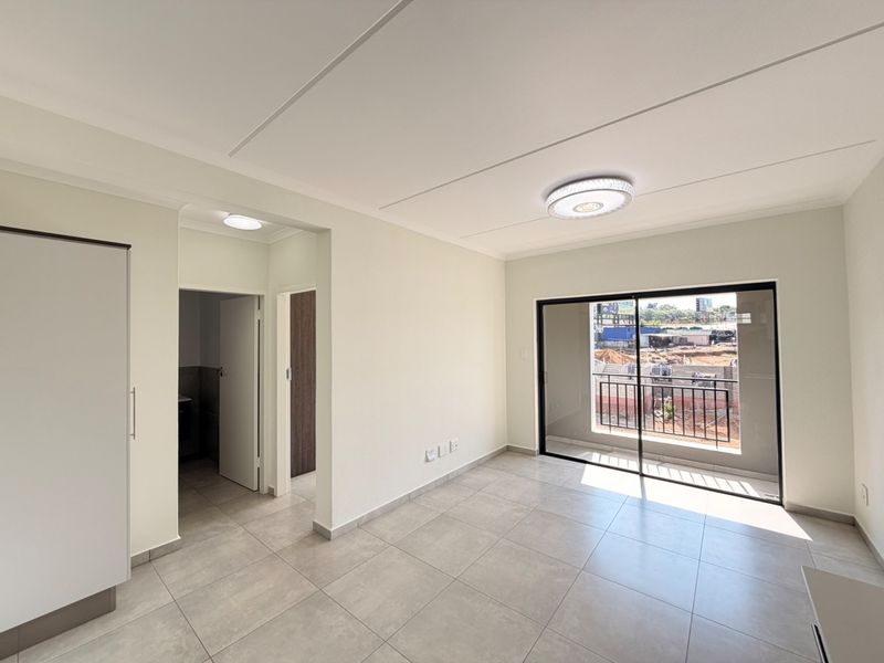 A bright, empty living area featuring neutral tiled flooring, a built-in cupboard, and a sliding glass door leading to a balcony.