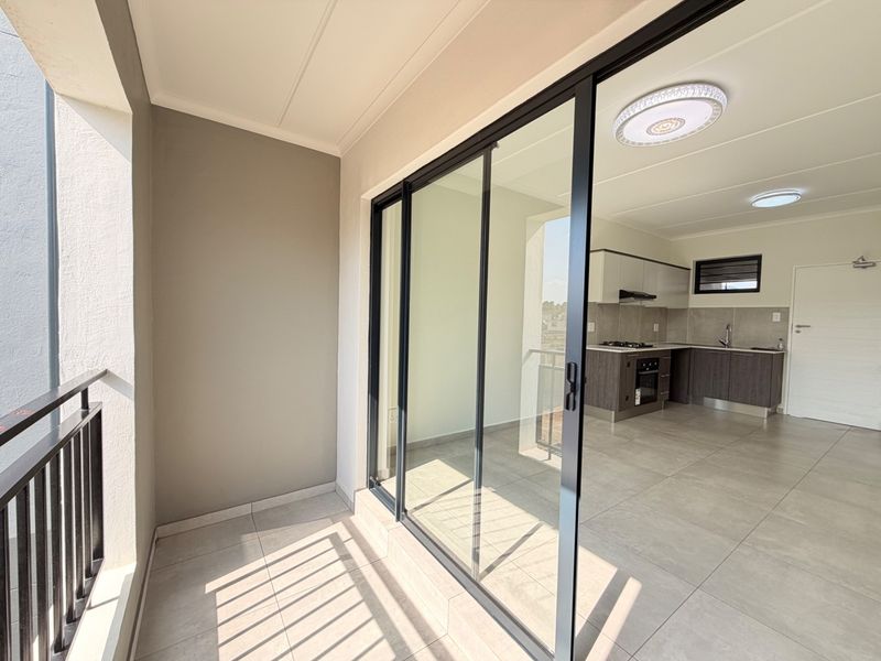 A modern balcony with tiled flooring and metal balustrade, providing seamless access to an open-plan kitchen area with contemporary cabinetry and built-in appliances.