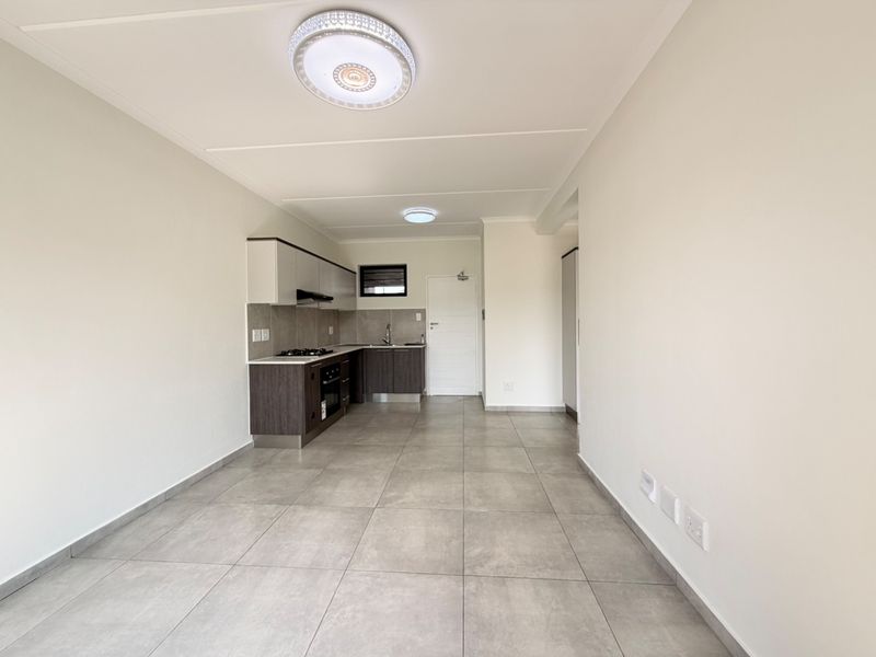 Modern open-plan kitchen and living area featuring neutral tiled flooring, contemporary cabinetry, and integrated cooking appliances in a clean, well-maintained space.