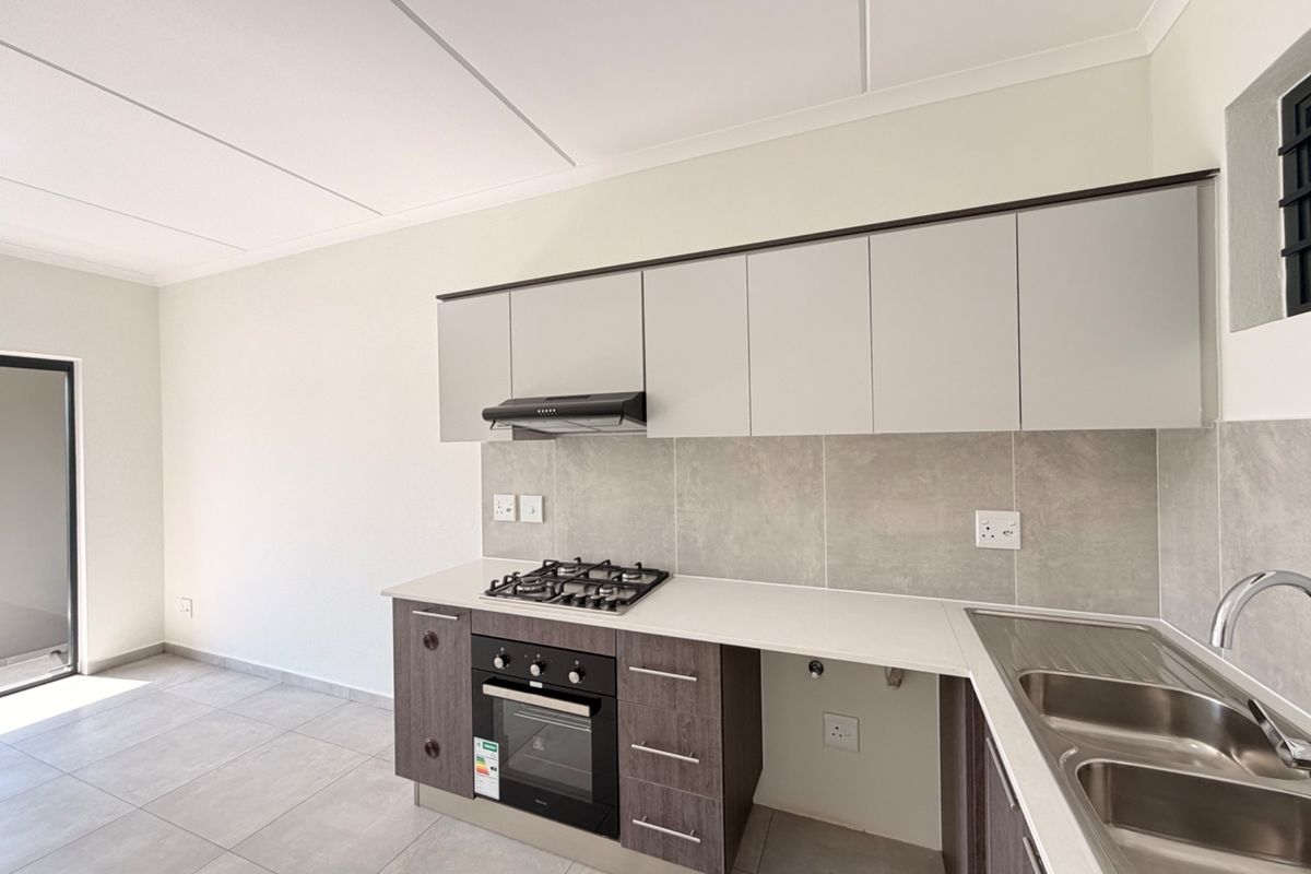 Modern kitchen featuring sleek cabinetry, built-in gas hob, oven, extractor fan, and stainless steel sink with neutral tiled finishes.
