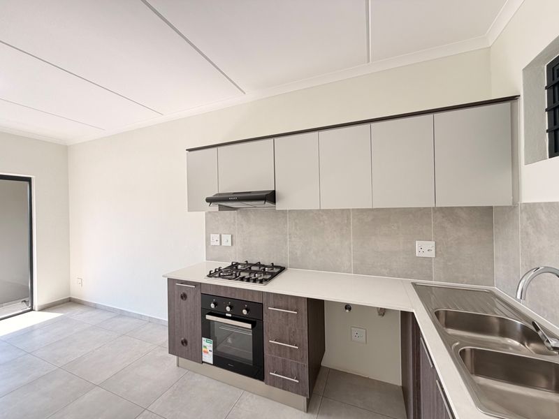 Modern kitchen featuring sleek cabinetry, built-in gas hob, oven, extractor fan, and stainless steel sink with neutral tiled finishes.