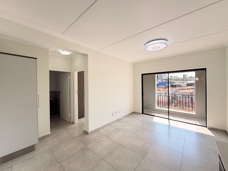 A bright, empty living area featuring neutral tiled flooring, a built-in cupboard, and a sliding glass door leading to a private balcony.