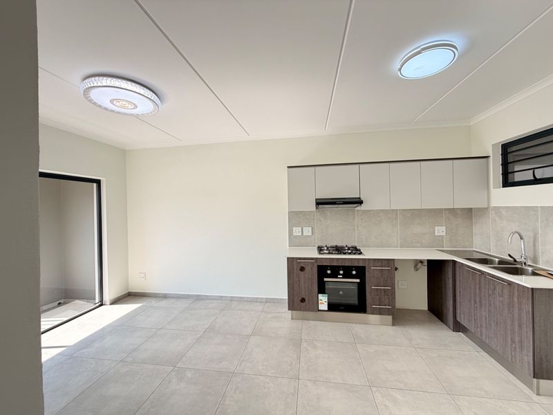 Modern open-plan kitchen featuring sleek cabinetry, gas hob, built-in oven, and tiled flooring, with direct access to an outdoor area.