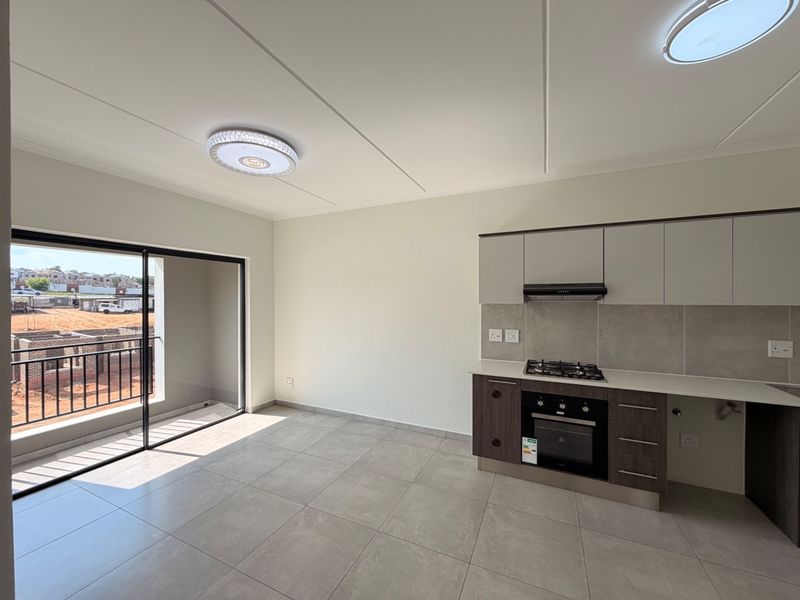 Modern open-plan kitchen and living area featuring tiled floors, built-in cabinetry with integrated appliances, and a sliding door leading to a private balcony.