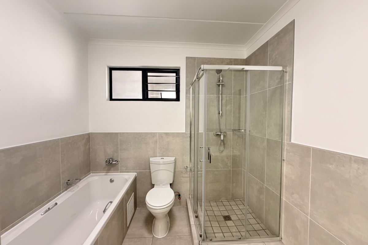 A modern, clean bathroom featuring a built-in bathtub, a separate glass-enclosed shower, and a toilet with neutral floor-to-ceiling tiling.