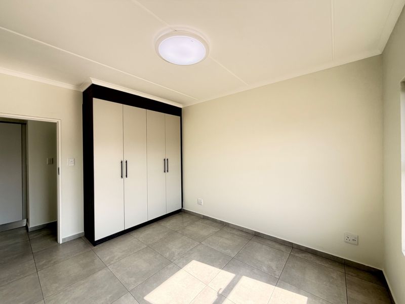 A clean, empty bedroom featuring neutral tiled flooring, a modern built-in wardrobe with dark framing, and a central ceiling light fixture.