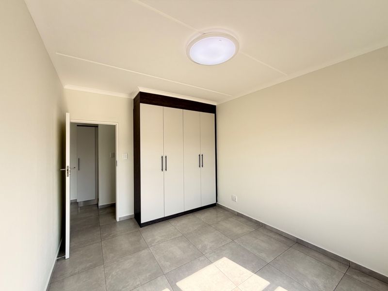 A clean, modern bedroom featuring neutral tiled flooring, built-in cupboards with dark trim, and a bright, minimalist aesthetic.