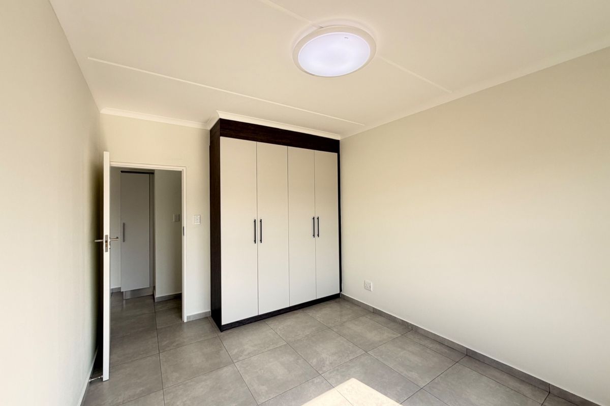 A clean, modern bedroom featuring neutral tiled flooring, built-in cupboards with dark trim, and a bright, minimalist aesthetic.