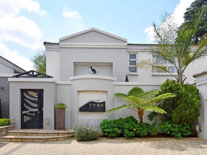 The front facade of the townhouse features a paved driveway, decorative metal entrance door, stone cladding accents, and well-maintained landscaping.