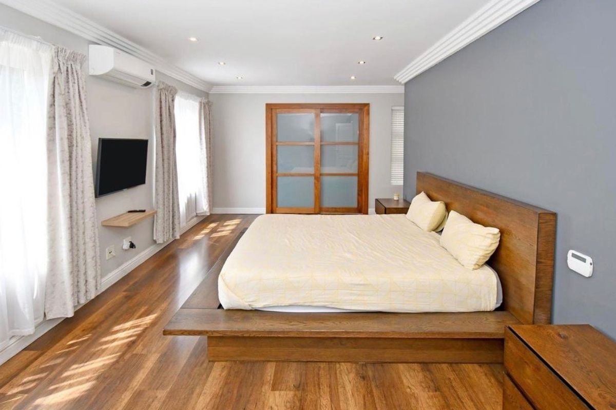 Spacious bedroom featuring hardwood flooring, crown molding, recessed lighting, and a built-in sliding door wardrobe with a wall-mounted air conditioning unit.