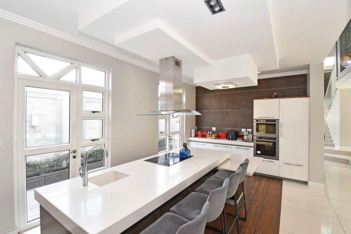Modern kitchen featuring a large central island with integrated hob, sleek cabinetry, built-in appliances, and direct access to an outdoor area.