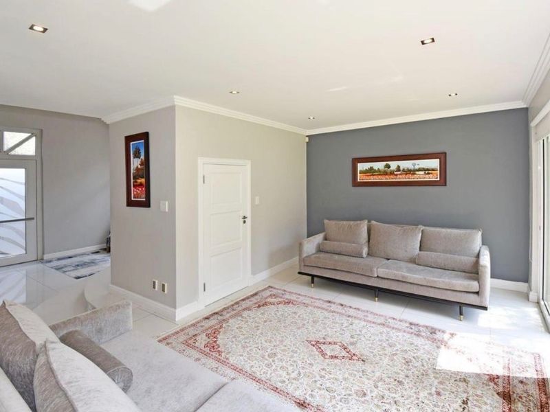 A bright and modern living room featuring neutral tones, tiled flooring, recessed downlighting, and a sliding glass door providing access to the exterior.