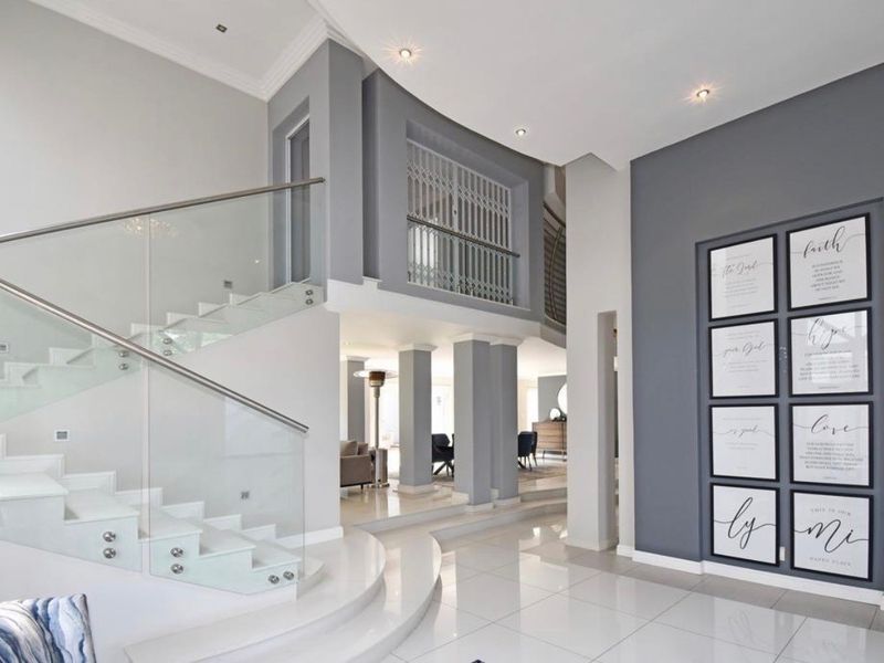Modern entrance hall featuring a striking glass-railed staircase, polished tiled flooring, and elegant architectural bulkhead ceilings with recessed lighting.
