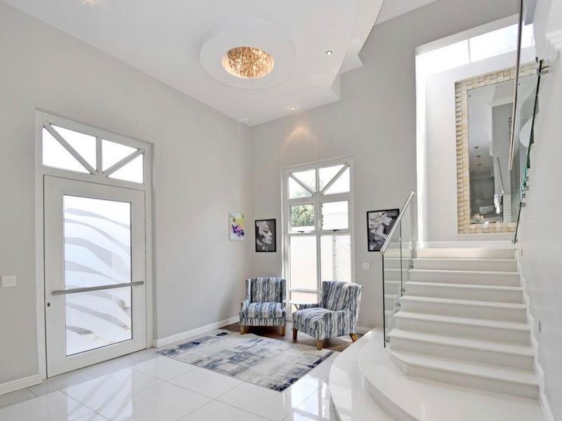A bright and modern entrance hall featuring high ceilings, polished tiled floors, and a contemporary staircase with a glass balustrade.