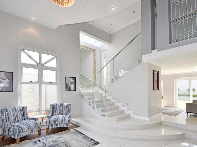 Spacious double-volume entrance hall featuring a modern glass balustrade staircase, high-quality tiled flooring, and abundant natural light from large windows.