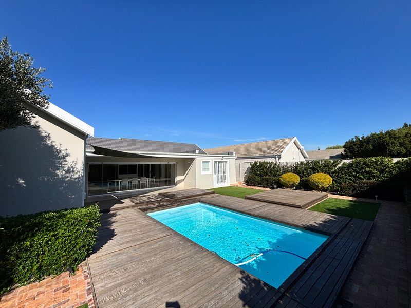 Outdoor pool area featuring timber decking, a shade sail, and direct access to the home through large sliding glass doors.