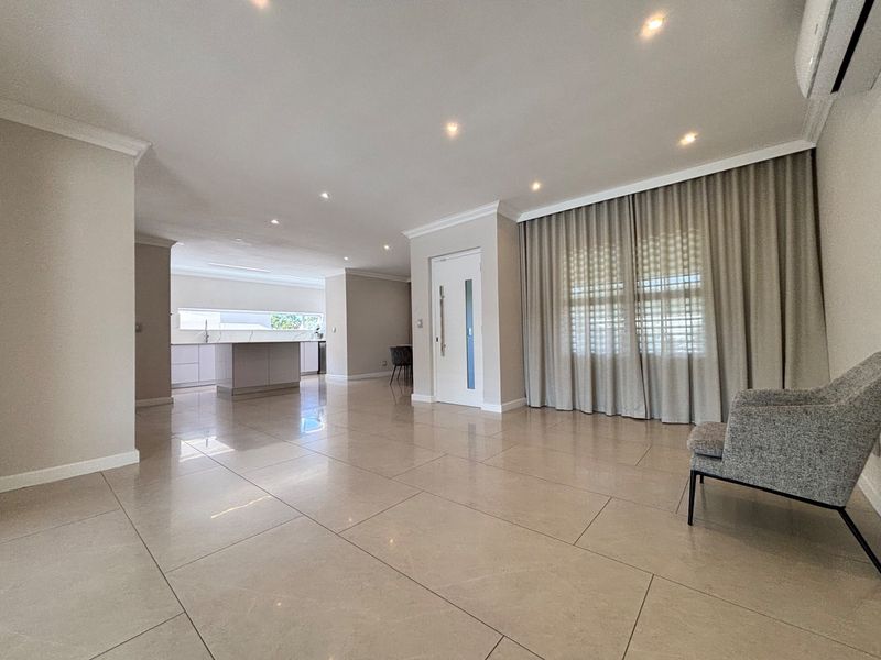 Spacious open-plan living area featuring large format porcelain tiles, recessed downlighting, and a modern kitchen with a central island.