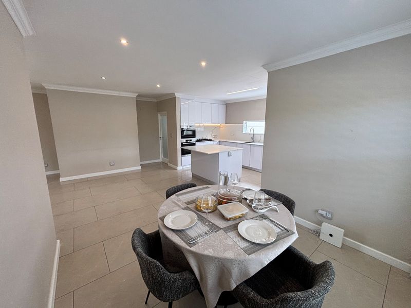Modern open-plan living and dining area featuring a sleek kitchen with a central island, built-in appliances, and neutral tiled flooring throughout.