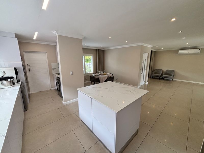 Spacious open-plan living area featuring a modern kitchen with a central island, quartz countertops, recessed lighting, and neutral tiled flooring throughout.
