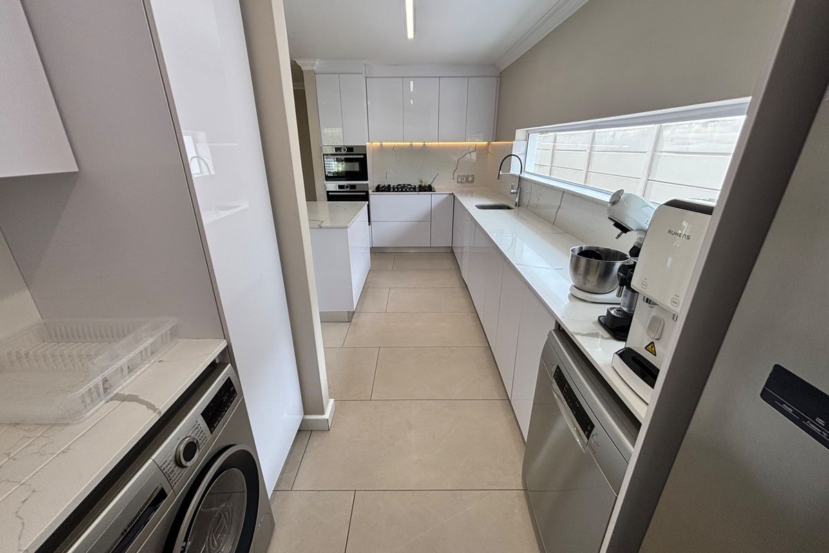 Modern, sleek kitchen featuring high-gloss cabinetry, stone countertops, integrated appliances, and a long horizontal window providing natural light.